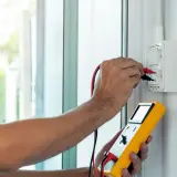 Elektryk mierzy impedancję pętli zwarcia za pomocą żółtego miernika.