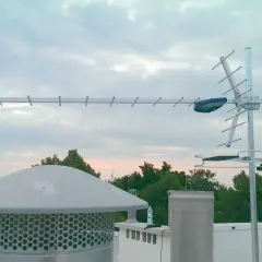 Antena telewizji naziemnej na dachu, na tle nieba i drzew.