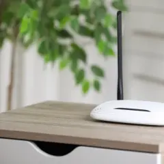 Biały router z dwiema antenami na drewnianym blacie. Dowiedz się, jak działa router bez karty SIM, tworząc domową sieć Wi-Fi.