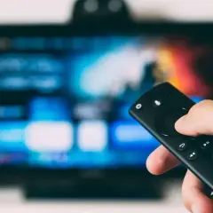 Dłoń trzymająca pilot do telewizora, ekran pokazuje menu. Dowiedz się, jak odbierać TV naziemną bez anteny, korzystając z nowoczesnych rozwiązań.