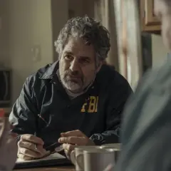 Detektyw FBI w kurtce z napisem FBI rozmawia z innymi osobami przy stole. Scena z seriali HBO Max.