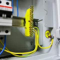 W skrzynce elektrycznej widać wyłączniki i żółto-zielone przewody tworzące uziemienie. Symbol uziemienia potwierdza bezpieczeństwo instalacji.