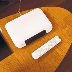 Biały router i pilot leżą na drewnianym stoliku. Chcesz wiedzieć, jak zmienić hasło do internetu Orange?