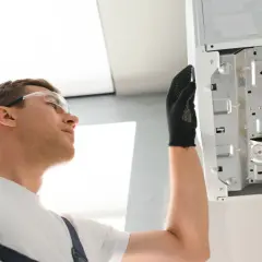 Instalator w okularach ochronnych sprawdza podłączenia kotła. Widać elementy takie jak anoda tytanowa i zawory.