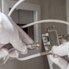 Ręce w białych rękawiczkach podłączają kabel antenowy do rozdzielacza.