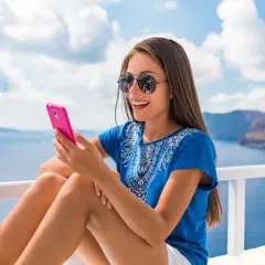 Uśmiechnięta kobieta z telefonem w ręku, ciesząca się widokiem morza. Czy na statku jest zasięg?