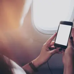 Ręce trzymające smartfon z pustym ekranem, siedząc przy oknie samolotu. Zastanawiasz się, czy bez karty SIM można dzwonić?