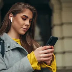 Kobieta z białymi słuchawkami bezprzewodowymi w uchu korzysta z telefonu Samsung. Dowiedz się, jak sparować słuchawki bezprzewodowe z telefonem Samsung.