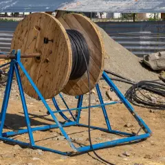 Drewniane bębny z kablem elektrycznym na niebieskim stojaku na placu budowy.