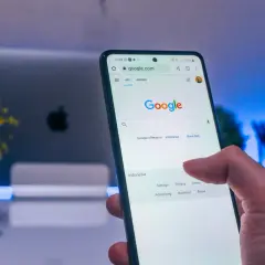 Palec dotyka ekranu telefonu z widoczną wyszukiwarką Google. Dowiedz się, jak wylogować się z konta Google, aby zwiększyć prywatność.