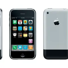 Trzy widoki pierwszego iPhone'a. Widoczny ekran z ikonami aplikacji, bok urządzenia oraz tył z logo Apple.