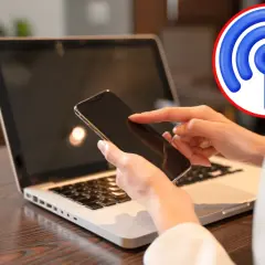 Jak udostępnić internet z telefonu na komputer przez USB? Dłoń z telefonem nad klawiaturą laptopa, symbol Wi-Fi.