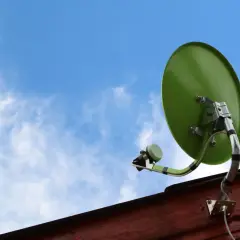 Zielona antena satelitarna zamontowana na drewnianej ścianie, gotowa do odbioru sygnału. Dowiedz się, jak zamontować antenę satelitarną.