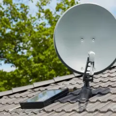 Antena satelitarna na dachu, obok okna dachowego. Prawidłowe ustawienie to klucz do tego, jak poprawić jakość sygnału satelitarnego.