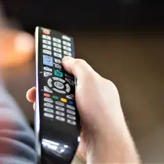 Dłoń trzyma pilot, zastanawiając się, czy telewizję naziemną można oglądać przez internet.