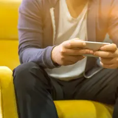 Mężczyzna siedzi na żółtym fotelu, trzymając telefon. Czy telefon bez karty SIM połączy się z Wi-Fi? Tak, to możliwe.