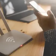 Router i osoba trzymająca telefon, zastanawiająca się, dlaczego wifi samo się wyłącza w telefonie.