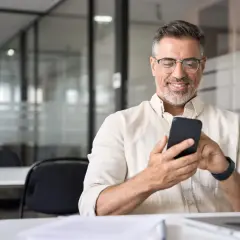Uśmiechnięty mężczyzna z telefonem w dłoni, szukający informacji, jak udostępnić internet z telefonu na laptopa.