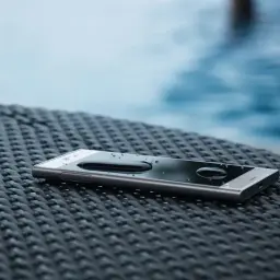 Telefon z kroplami wody na ekranie, leżący na plecionej powierzchni. IP68 co oznacza? Wodoodporność i pyłoszczelność.