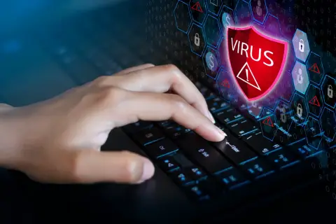 Dłoń naciska klawisz Enter na klawiaturze, symbolizując walkę z zagrożeniem. Ikona tarczy z napisem "VIRUS" i wykrzyknikiem sugeruje, jak usunąć wirusa z komputera.