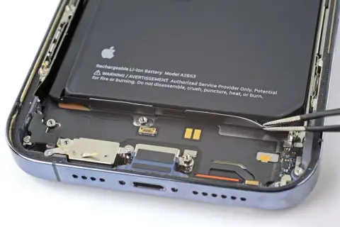 Wymiana baterii iPhone 14 Pro w toku. Pęseta odłącza taśmę baterii.