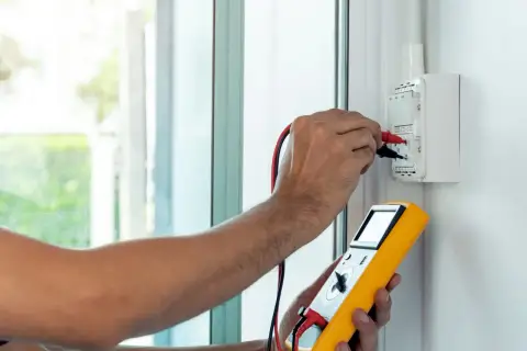 Elektryk mierzy impedancję pętli zwarcia za pomocą żółtego miernika.