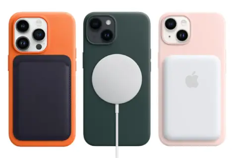 Trzy iPhone'y 14 w kolorowych etui: pomarańczowym z portfelem, zielonym z ładowarką MagSafe i różowym z powerbankiem. Premiera iPhone 14.