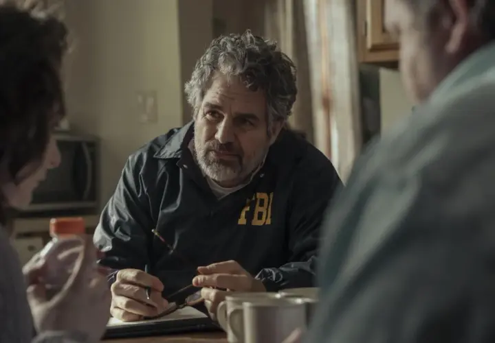Detektyw FBI w kurtce z napisem FBI rozmawia z innymi osobami przy stole. Scena z seriali HBO Max.