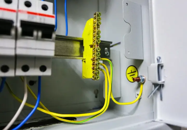 W skrzynce elektrycznej widać wyłączniki i żółto-zielone przewody tworzące uziemienie. Symbol uziemienia potwierdza bezpieczeństwo instalacji.