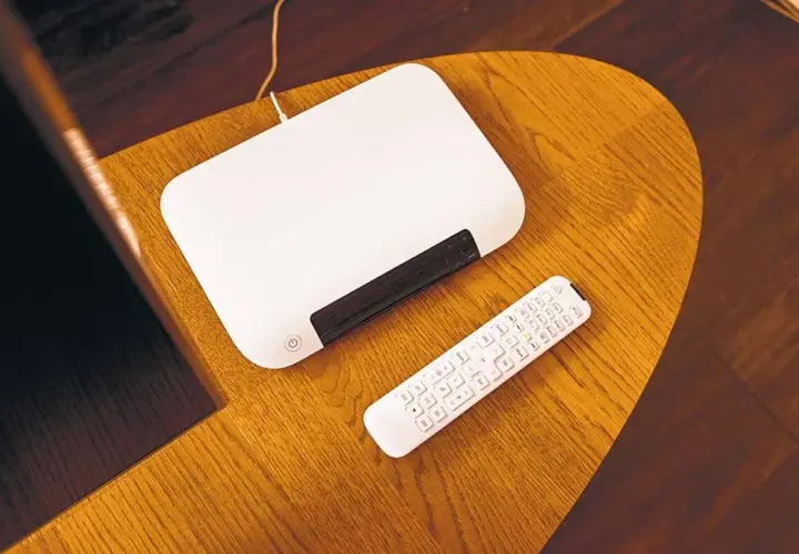 Biały router i pilot leżą na drewnianym stoliku. Chcesz wiedzieć, jak zmienić hasło do internetu Orange?