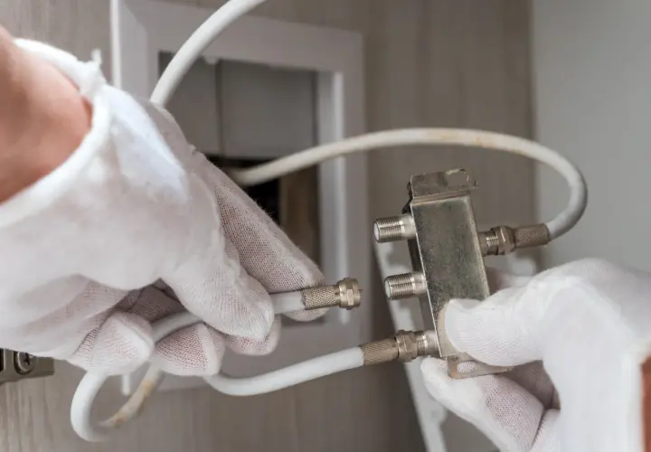 Ręce w białych rękawiczkach podłączają kabel antenowy do rozdzielacza.