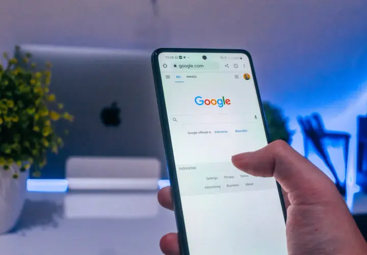 Palec dotyka ekranu telefonu z widoczną wyszukiwarką Google. Dowiedz się, jak wylogować się z konta Google, aby zwiększyć prywatność.
