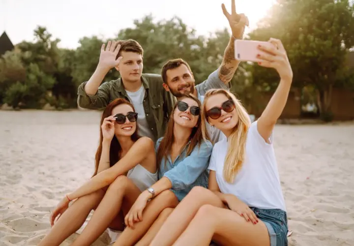 Grupa przyjaciół robi selfie na plaży. Zastanawiasz się, jak sprawdzić, czy roaming jest włączony Plus abonament? Sprawdź to przed wyjazdem!
