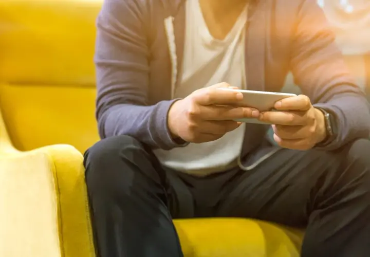 Mężczyzna siedzi na żółtym fotelu, trzymając telefon. Czy telefon bez karty SIM połączy się z Wi-Fi? Tak, to możliwe.