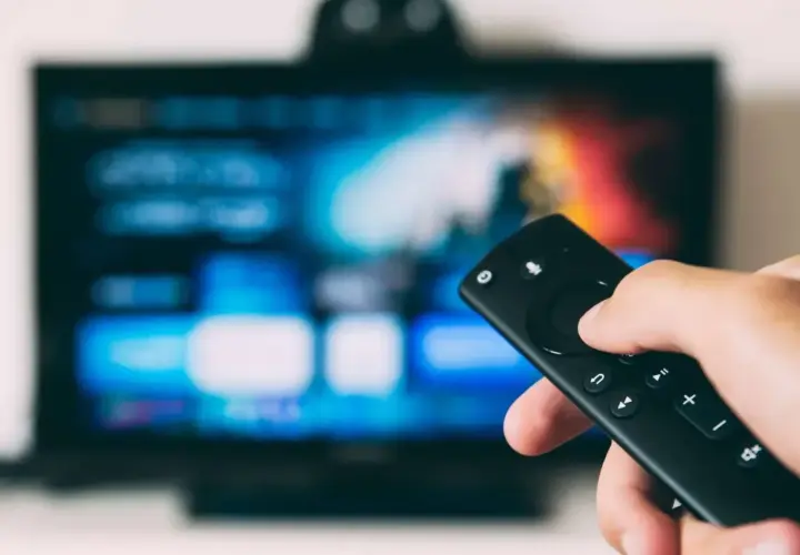 Dłoń trzymająca pilot do telewizora, ekran pokazuje menu. Dowiedz się, jak oglądać TV naziemną przez internet.