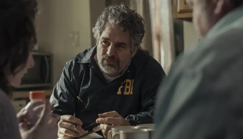 Detektyw FBI w kurtce z napisem FBI rozmawia z innymi osobami przy stole. Scena z seriali HBO Max.