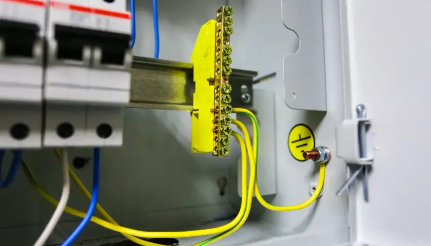 W skrzynce elektrycznej widać wyłączniki i żółto-zielone przewody tworzące uziemienie. Symbol uziemienia potwierdza bezpieczeństwo instalacji.