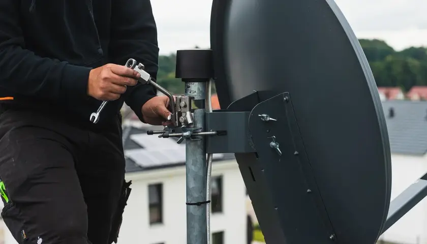 Instalator dokręca śruby przy antenie satelitarnej, pokazując jak ustawić antenę satelitarną cyfrowego polsatu.