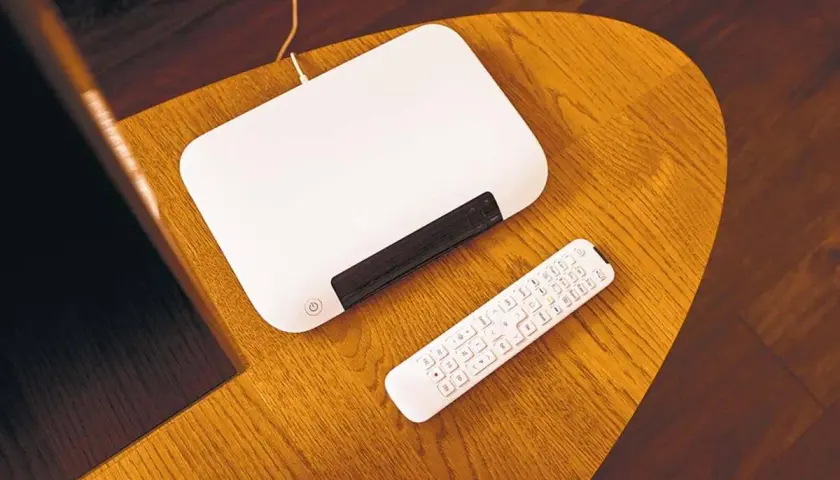 Biały router i pilot leżą na drewnianym stoliku. Chcesz wiedzieć, jak zmienić hasło do internetu Orange?
