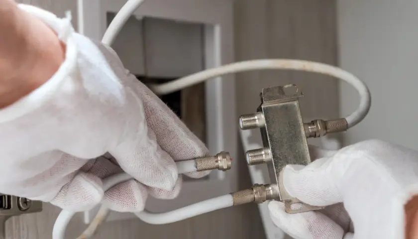 Ręce w białych rękawiczkach podłączają kabel antenowy do rozdzielacza.