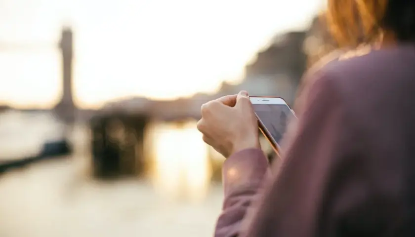 Osoba sprawdza na telefonie, jak włączyć roaming w Orange na kartę, podczas zachodu słońca nad wodą.