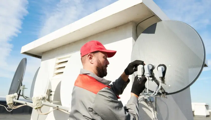 Technik w czerwonej czapce reguluje konwerter anteny satelitarnej. To kluczowy etap, jak zrobić antenę satelitarną, by odbierać sygnał.