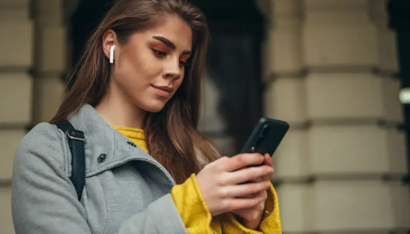 Kobieta z białymi słuchawkami bezprzewodowymi w uchu korzysta z telefonu Samsung. Dowiedz się, jak sparować słuchawki bezprzewodowe z telefonem Samsung.