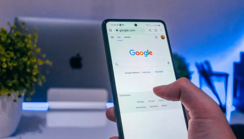 Palec dotyka ekranu telefonu z widoczną wyszukiwarką Google. Dowiedz się, jak wylogować się z konta Google, aby zwiększyć prywatność.
