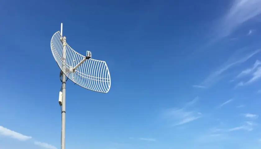 Siatkowa antena telewizyjna na tle błękitnego nieba z chmurami.