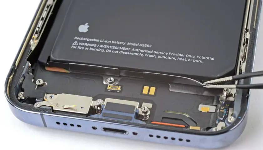 Wymiana baterii iPhone 14 Pro w toku. Pęseta odłącza taśmę baterii.