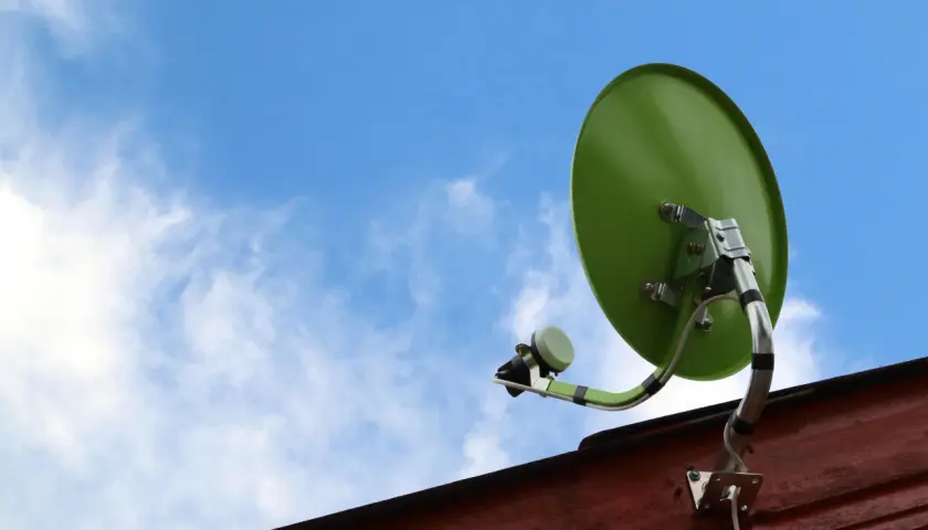 Zielona antena satelitarna zamontowana na drewnianej ścianie, gotowa do odbioru sygnału. Dowiedz się, jak zamontować antenę satelitarną.