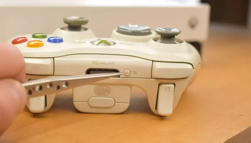 Pęseta zbliża się do przycisku synchronizacji na białym padzie Xbox. Dowiedz się, jak podłączyć drugiego pada Xbox.