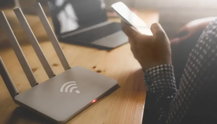 Router i osoba trzymająca telefon, zastanawiająca się, dlaczego wifi samo się wyłącza w telefonie.