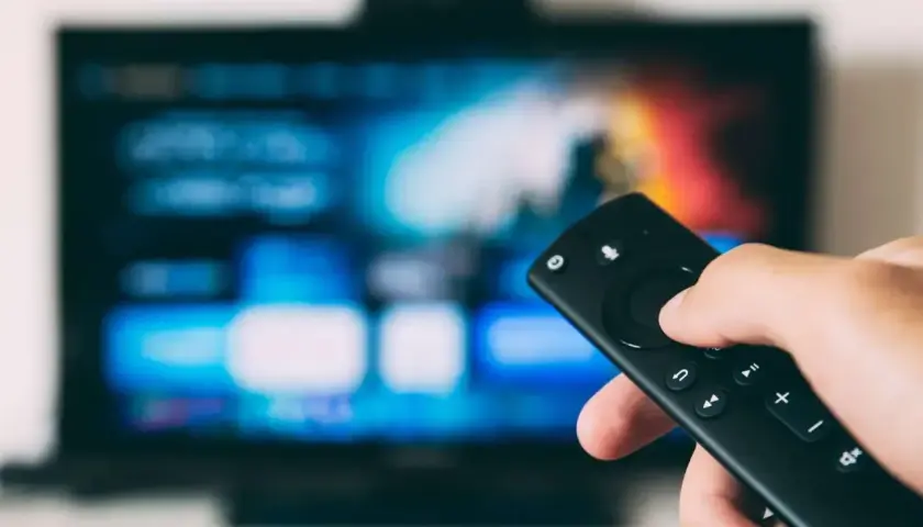 Dłoń trzymająca pilot do telewizora, ekran pokazuje menu. Dowiedz się, jak oglądać TV naziemną przez internet.